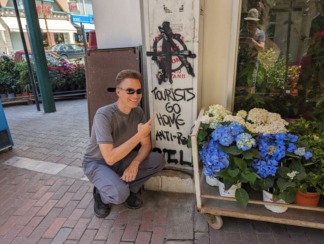 The author next to anti-tourist graffiti in the Vyronas neighborhood of Athens in 2022. 